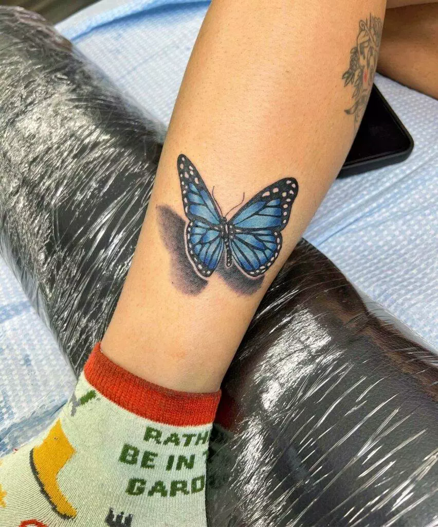 A blue butterfly tattoo on a woman's leg.