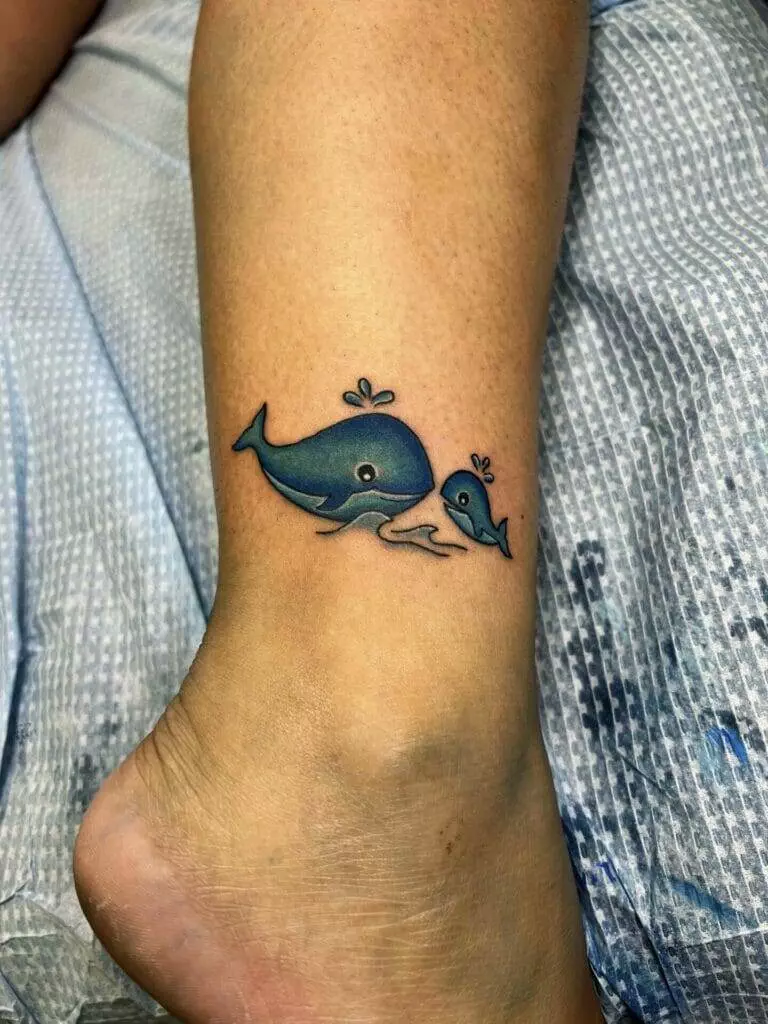 A woman's ankle with a tattoo of a whale and a baby whale.