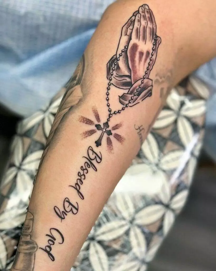 A tattoo with a rosary and praying hands.