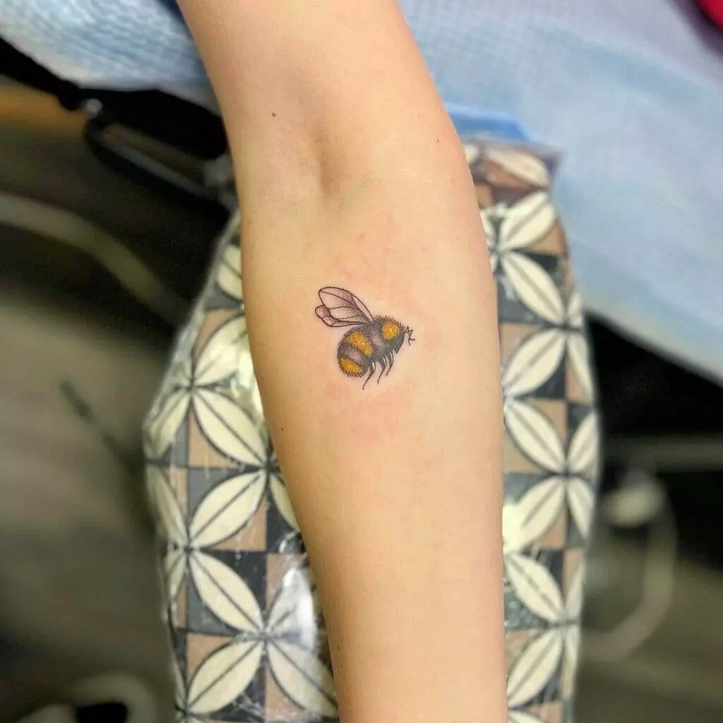 A small bee tattoo on a woman's forearm.