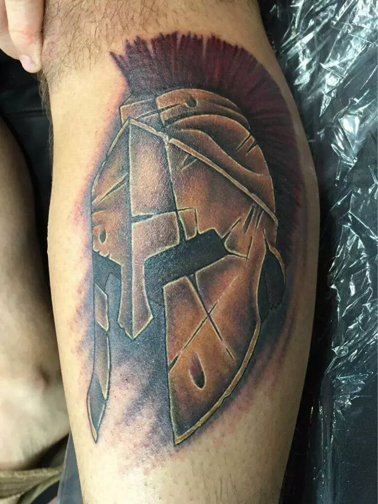 A spartan helmet tattoo on a man's leg.