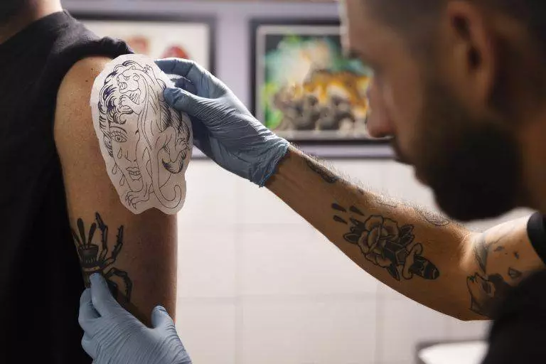 In a San Diego tattoo studio, the artist expertly places a lion stencil on a client's arm, with framed art creating an inspiring backdrop.