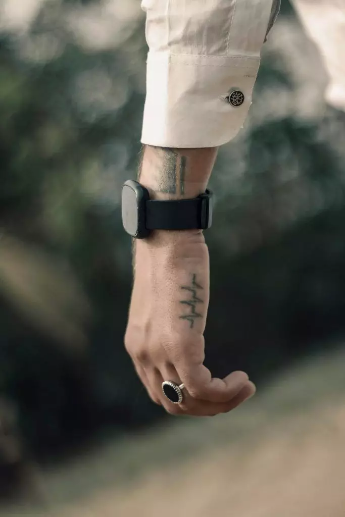 A person's wrist with a smart watch, a tattoo on the hand—a striking piece from the tattoo industry—a ring on the ring finger, and a white shirt cuff with a cufflink.