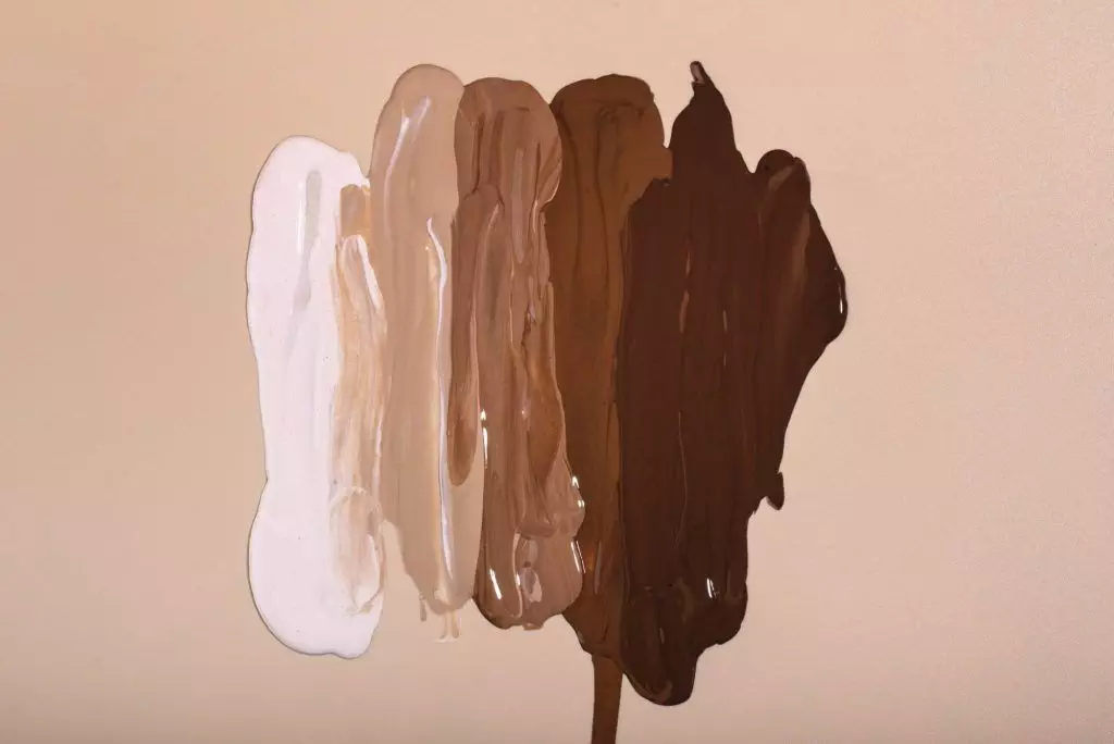 Five vertical swatches of foundation in varying shades from light to dark, applied on a beige background, showcasing the essence of Ink Perfection.