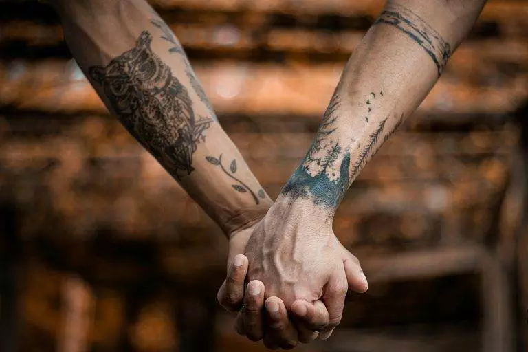 Close-up of tattooed hands holding each other, symbolizing connection and affection.